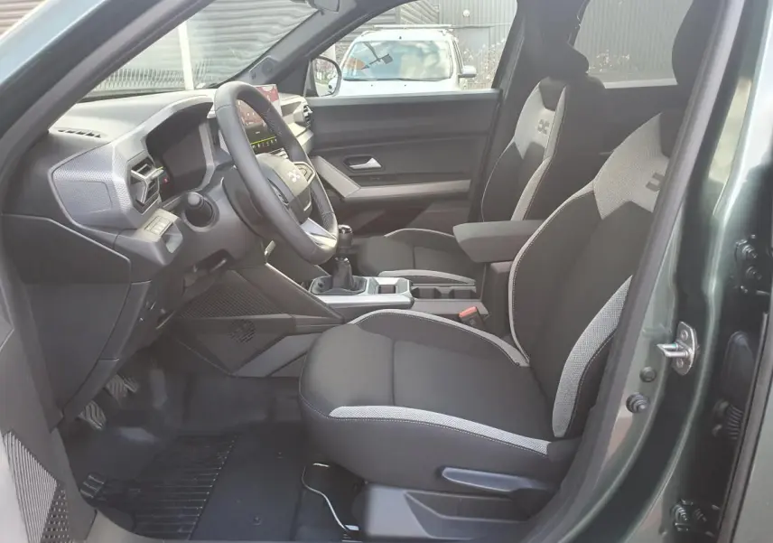Intérieur du Dacia Duster 2026 vert cèdre, vue côté conducteur, sièges tissu bicolore et tableau de bord moderne.