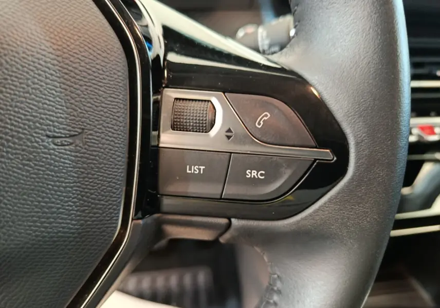 Gros plan sur les commandes gauche du volant cuir noir de la Peugeot 208 blanche PureTech 100 S&S Allure Business 2021.