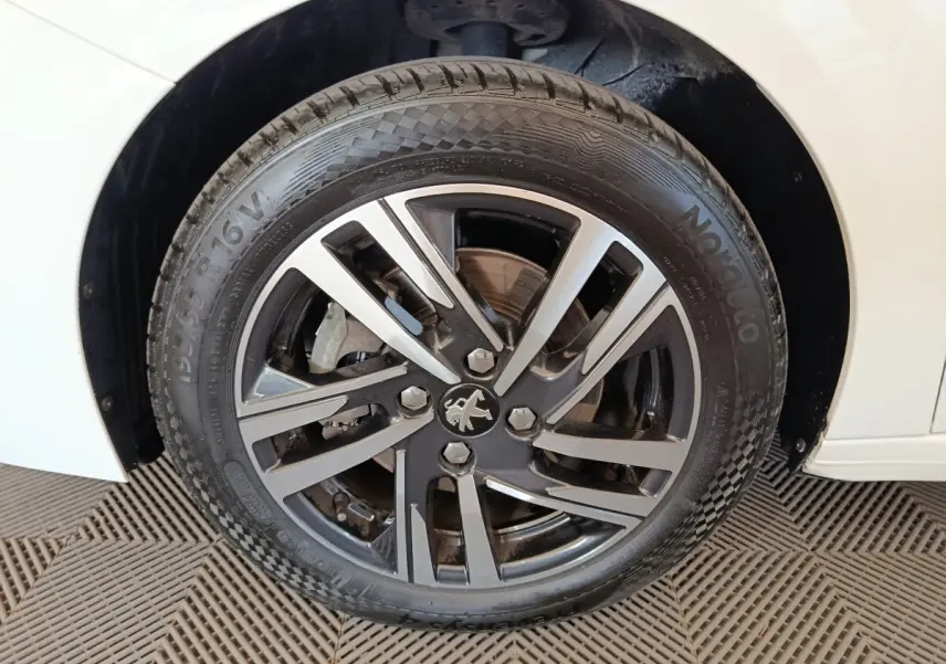 Gros plan sur la roue avant gauche de la Peugeot 208 blanche, mettant en valeur la jante alliage au design moderne.