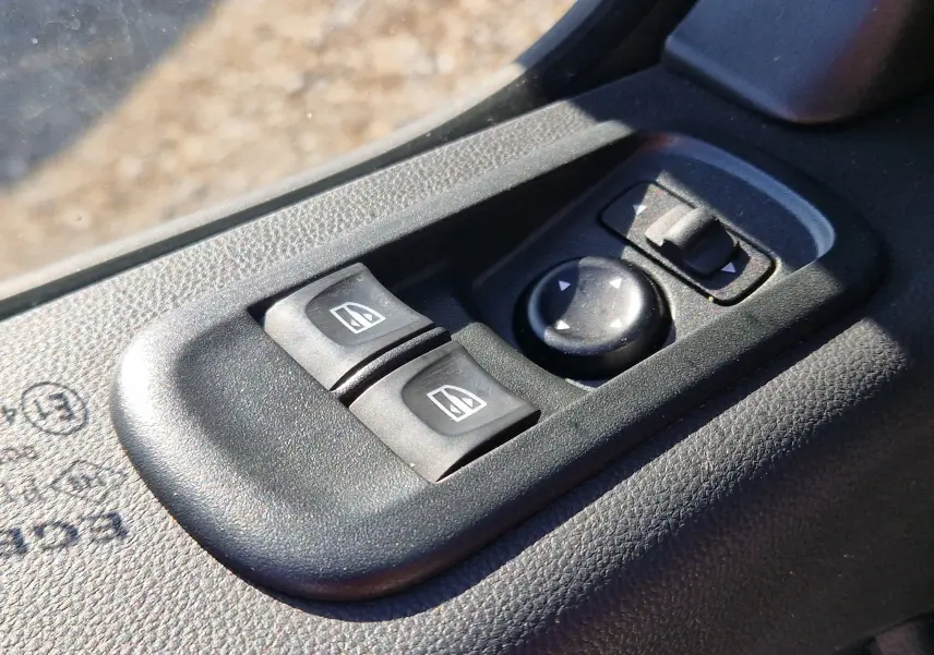 Gros plan sur les commandes de lève-vitres et réglage des rétroviseurs côté conducteur d’un Renault Master blanc.