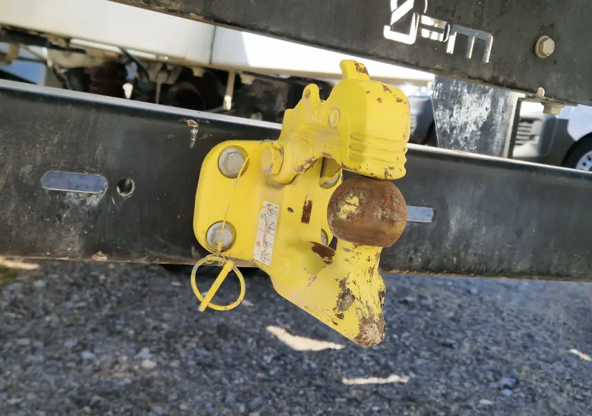 Gros plan sur l'attelage jaune rouillé fixé au châssis arrière noir d'un Renault Master blanc.