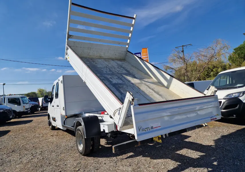 Vue 3/4 arrière droite d’un Renault Master blanc avec benne relevée et coffre, roues jumelées visibles au soleil.