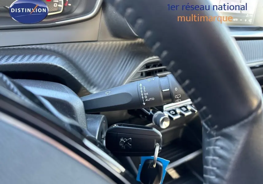Gros plan sur la clé de contact Peugeot 2008 gris Artense insérée près du volant et des commandes d'essuie-glace.