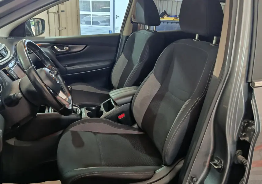 Vue intérieure côté conducteur du Nissan Qashqai gris clair 2019, montrant les sièges avant en tissu noir et le volant multi-fonctions.