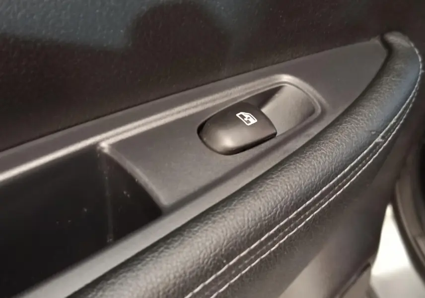 Détail du bouton de commande de la vitre électrique sur la porte intérieure en cuir noir du Nissan Qashqai gris clair.