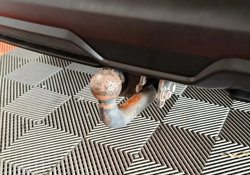 Gros plan sur la boule d'attelage rouillée sous le pare-chocs arrière d'un Nissan Qashqai gris clair.