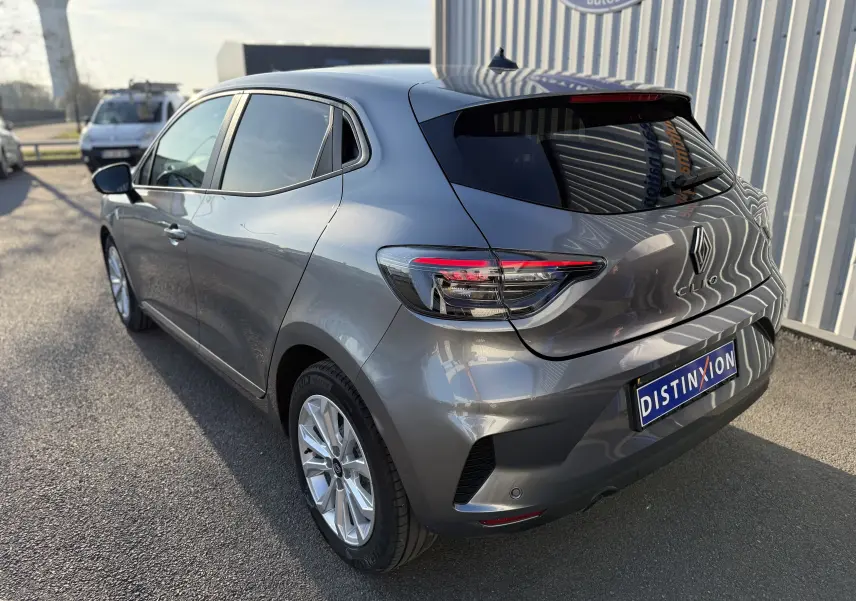 Vue 3/4 arrière droite d'une Renault Clio V gris schiste métal avec feux LED et jantes alliage sur parking extérieur.