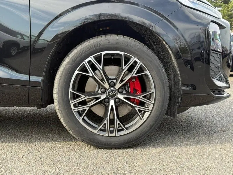 Gros plan sur la roue avant gauche d’un Audi Q3 2026 noir Mythique métallisé avec étrier de frein rouge et jante S line.