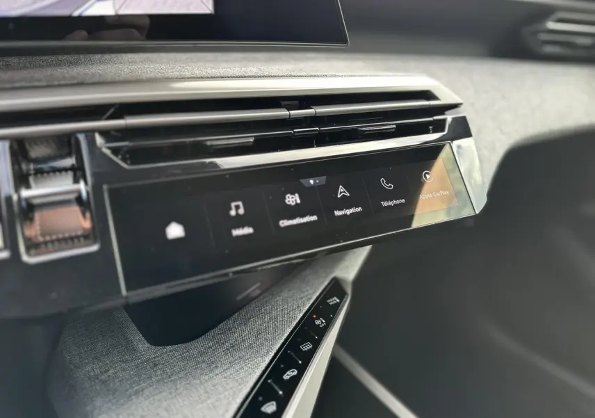 Vue rapprochée de la console centrale du Peugeot 3008 Hybrid 2025 avec écran tactile panoramique et commandes tactiles sur tissu gris.