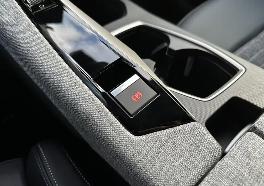 Gros plan sur la console centrale tissu gris chiné du Peugeot 3008 Hybrid 2025 avec bouton frein électrique rouge.