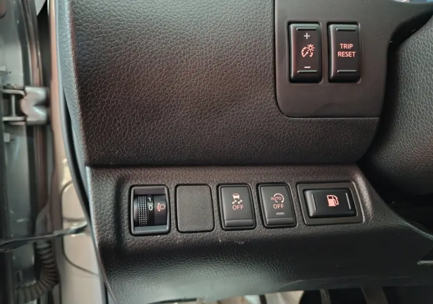 Gros plan sur les commandes côté gauche du tableau de bord du Nissan Navara gris clair, avec boutons de réglage des phares et traction.