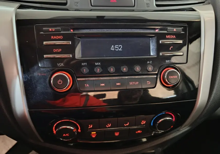 Vue rapprochée du tableau de bord noir du Nissan Navara 2018 avec commandes audio et climatisation éclairées en rouge.