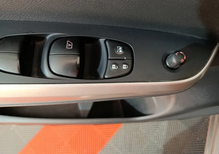 Gros plan sur la commande des vitres et rétroviseurs côté conducteur du Nissan Navara gris clair, intérieur noir.