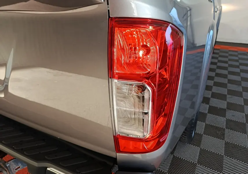 Gros plan sur le feu arrière droit rouge et blanc du Nissan Navara gris clair, avec marchepied noir visible dessous.
