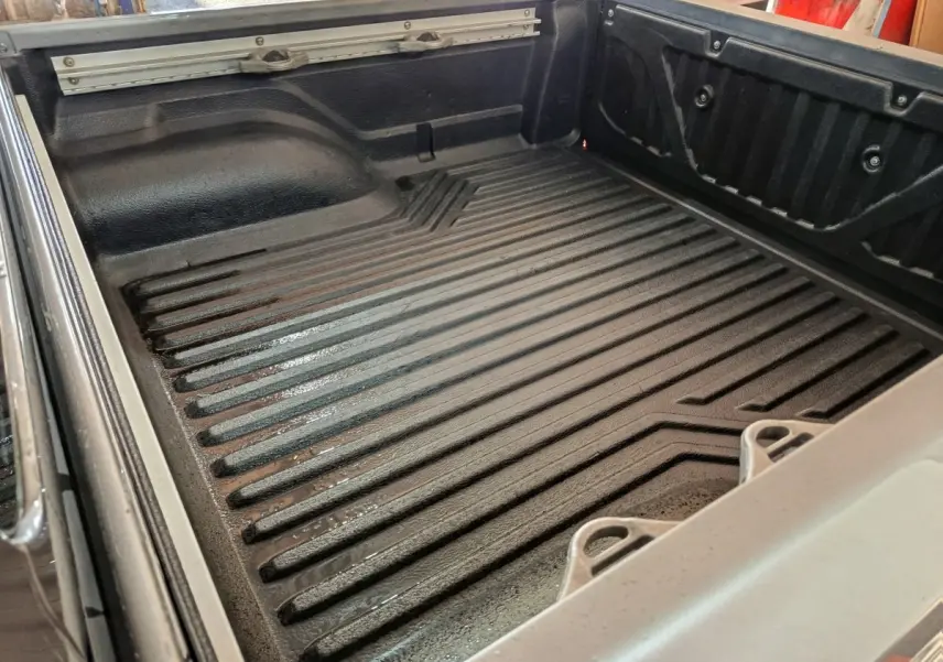 Vue rapprochée de la benne noire du Nissan Navara gris clair, montrant les ridules et crochets de retenue.