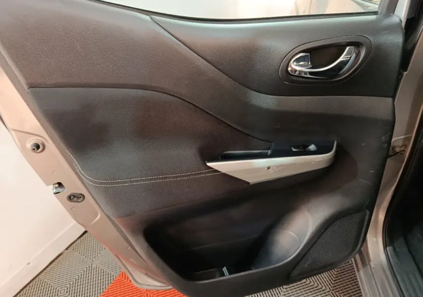 Vue intérieure de la porte avant gauche du Nissan Navara gris clair, avec poignée chrome et panneau noir texturé.