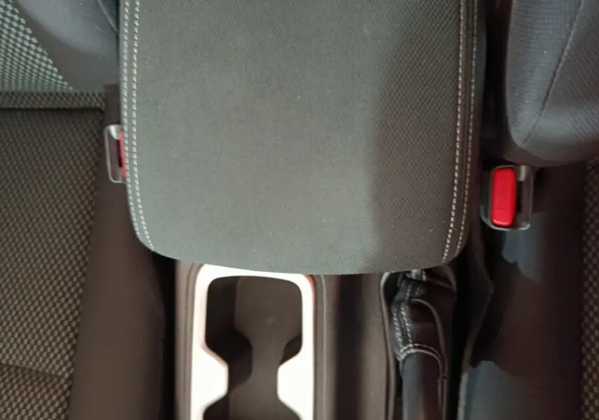 Vue plongeante sur la console centrale noire du Nissan Navara avec accoudoir, frein à main et porte-gobelets.