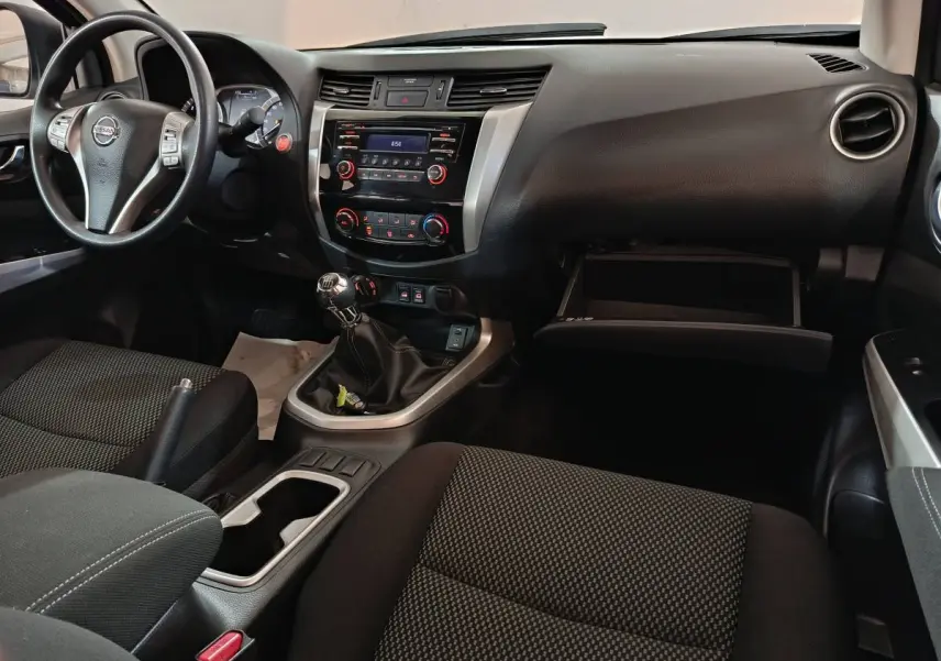Vue intérieure côté conducteur du Nissan Navara 2018, montrant tableau de bord noir, volant multifonctions et boîte manuelle.