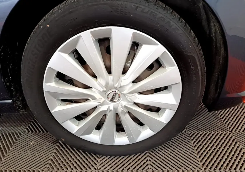 Gros plan sur la roue avant droite d’une Nissan Micra gris foncé avec enjoliveur argenté et logo central Nissan.