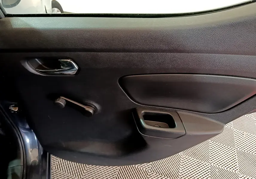 Vue intérieure du panneau de porte côté conducteur d'une Nissan Micra gris foncé, avec poignée chromée et commande manuelle de vitre.