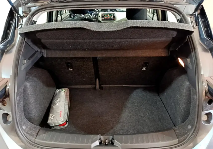 Coffre ouvert d'une Nissan Micra gris foncé, vue arrière montrant l'espace de chargement et un kit de secours.