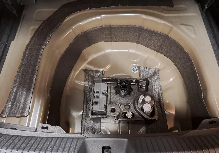 Vue rapprochée du coffre ouvert du Volkswagen Taigo 2025, montrant le logement pour roue de secours et kit de dépannage.