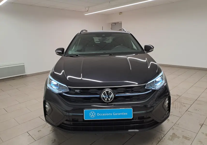 Vue avant du Volkswagen Taigo noir intense nacré avec calandre R-Line et projecteurs LED allumés dans un showroom.