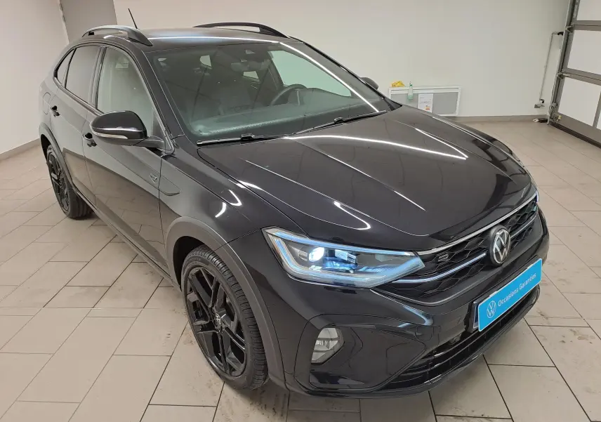 Volkswagen Taigo 1.5 TSI R-Line noir intense nacré, vue 3/4 avant avec jantes noires 18 pouces et phares LED allumés.