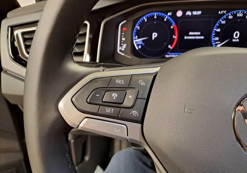 Gros plan sur la partie gauche du volant cuir du Volkswagen Taigo 2025 avec commandes de régulateur de vitesse et tableau de bord digital.