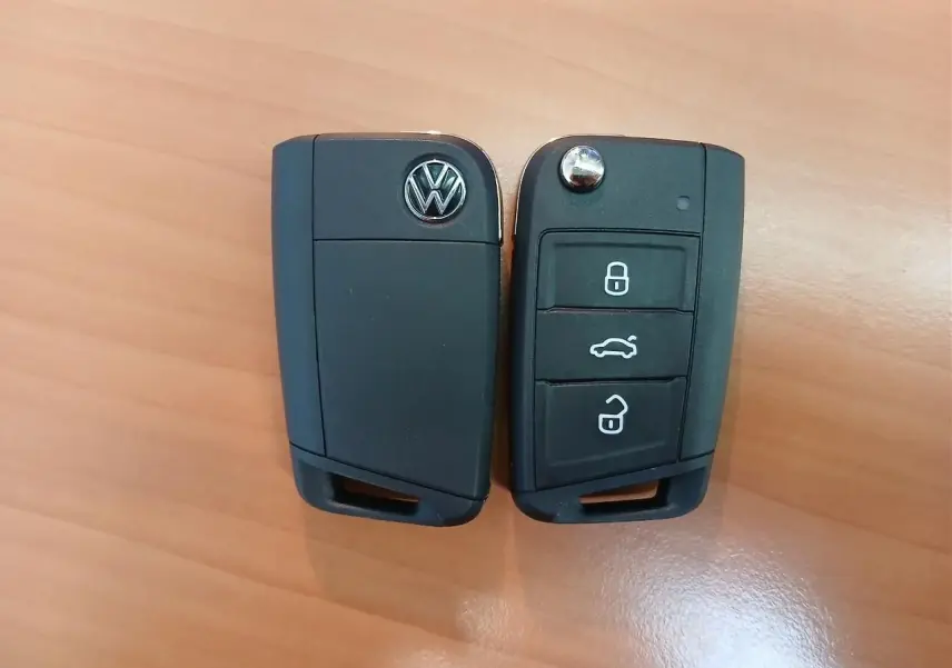 Vue rapprochée de deux clés noires Volkswagen avec boutons de verrouillage et logo sur fond bois clair.