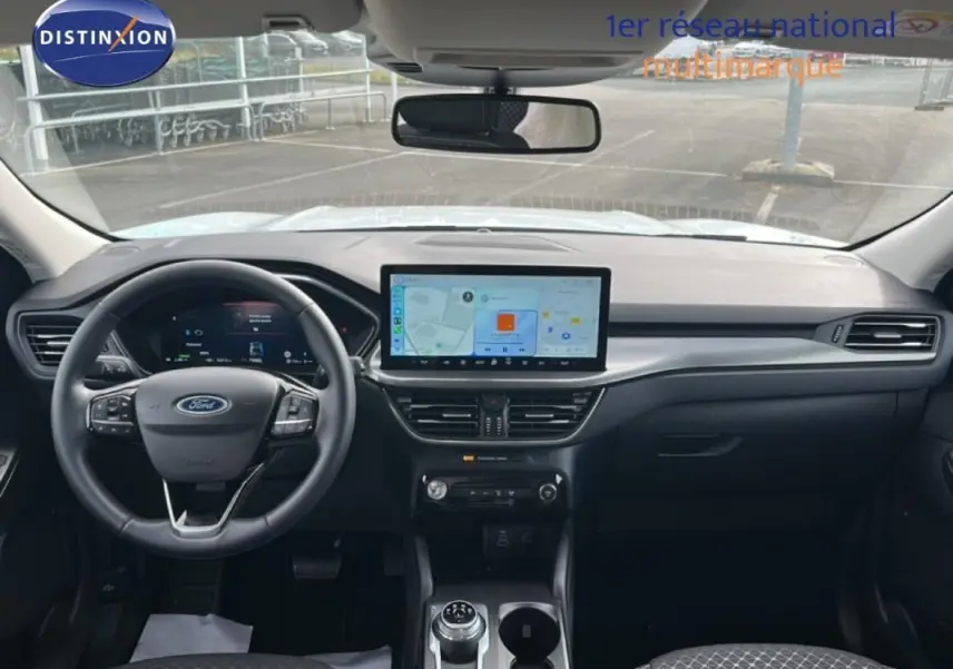 Vue intérieure frontale du tableau de bord noir du Ford Kuga blanc 2025 avec écran tactile central et volant multifonction.