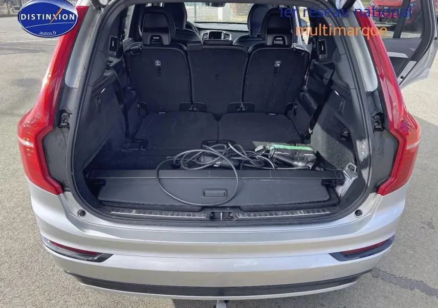 Coffre ouvert d'un Volvo XC90 gris 3/4 arrière, montrant l'espace de chargement avec câbles de recharge hybride.