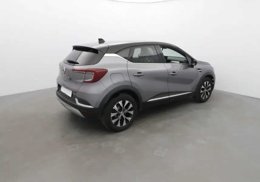 Vue 3/4 arrière droite d'un Renault Captur 2024 gris Cassiopée avec toit noir et jantes alliage bicolores.