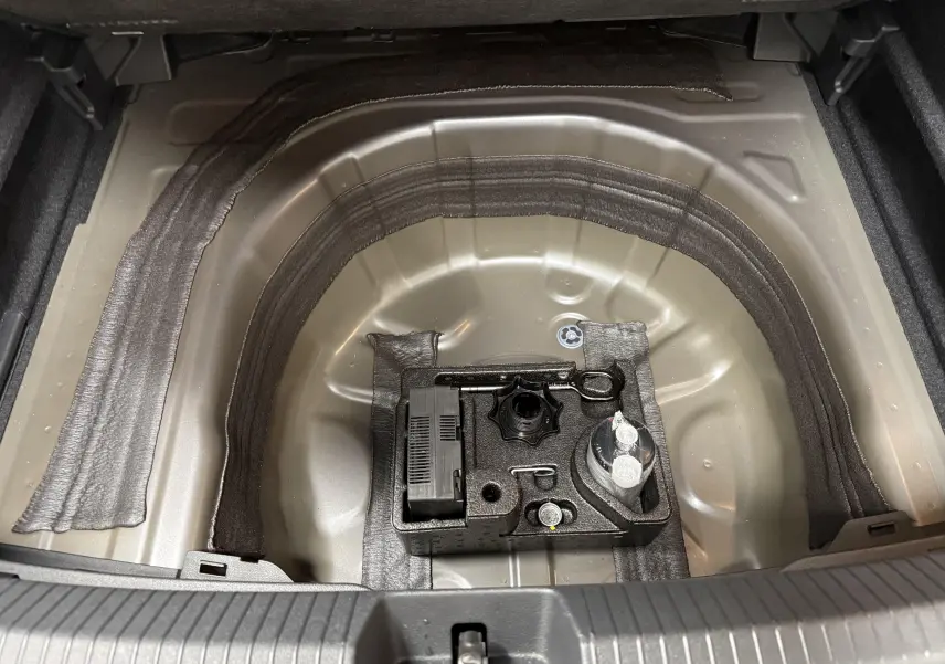 Vue plongeante sur le coffre ouvert du Volkswagen Taigo gris cendre, montrant le rangement pour roue de secours et outils.