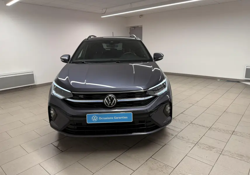 Vue avant d'un Volkswagen Taigo gris cendre R-Line Edition avec calandre noire et phares LED allumés dans un showroom.