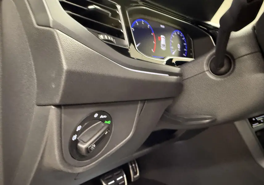 Vue intérieure côté gauche du tableau de bord gris foncé du Volkswagen Taigo avec commandes d'éclairage et combiné d'instruments digital.