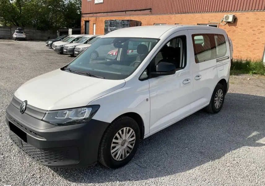 Volkswagen Caddy blanc Candy vue 3/4 avant droit, avec pare-chocs noir et portes coulissantes visibles.