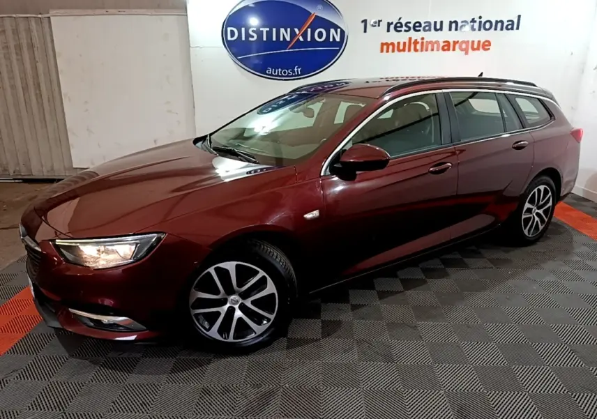 Opel Insignia break rouge vue 3/4 avant droit avec phares allumés dans un showroom intérieur.