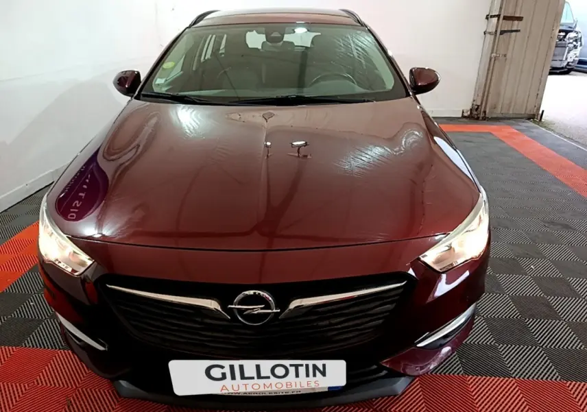 Vue avant d'une Opel Insignia rouge 2019 avec calandre noire et phares allumés dans un garage.