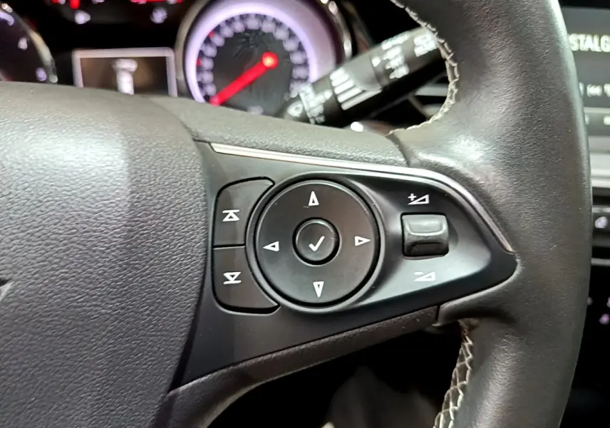 Gros plan sur les commandes multifonctions noires du volant cuir de l’Opel Insignia 2019, tableau de bord en arrière-plan.
