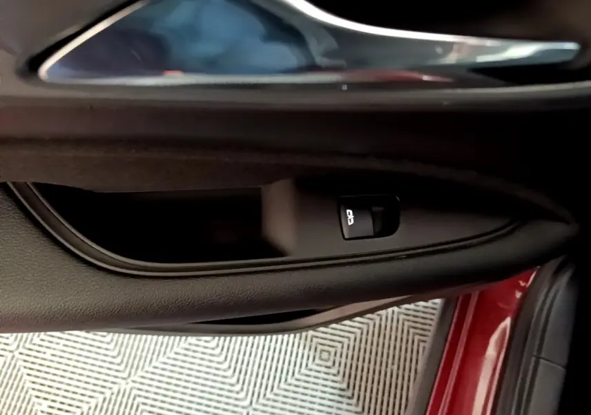 Gros plan sur la poignée intérieure et bouton de verrouillage de la porte côté conducteur d’une Opel Insignia rouge.