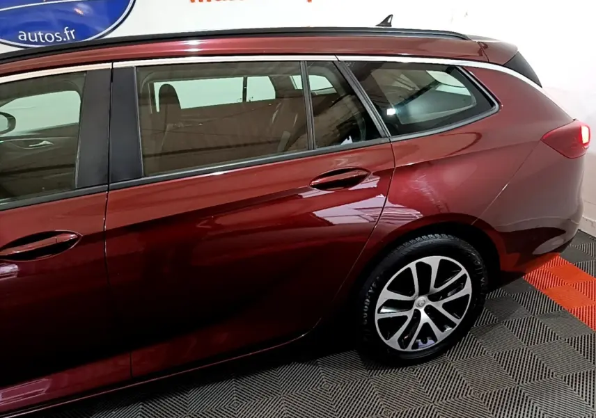 Vue latérale côté droit d'une Opel Insignia break rouge métallisé, mettant en valeur les jantes alliage et la ligne fluide du toit.