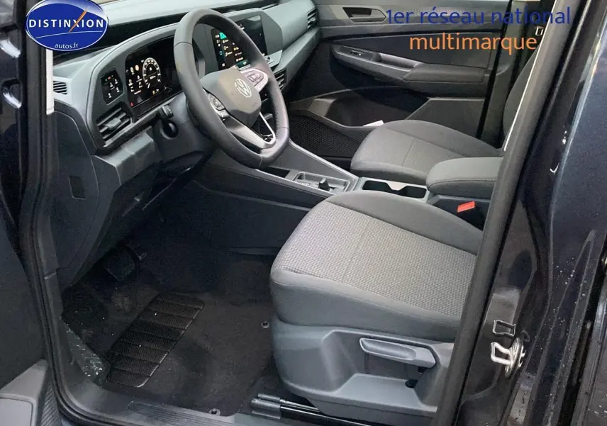 Vue intérieure côté conducteur du Volkswagen Caddy 2025 bleu métallisé, avec sièges tissu noir et tableau de bord moderne.