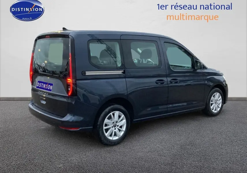 Volkswagen Caddy bleu métallisé vu de profil droit, avec feux arrière verticaux allumés et jantes argentées.