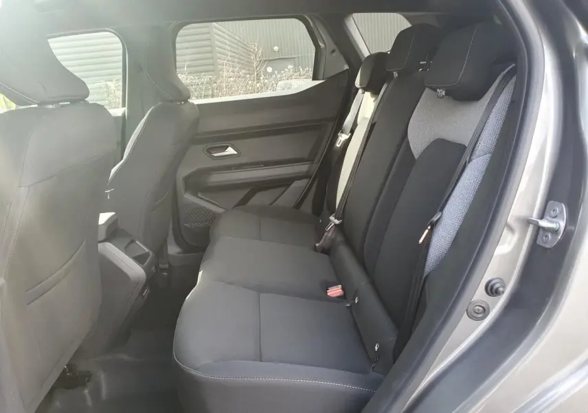 Vue intérieure côté droit sur la banquette arrière noire du Dacia Dokker Van gris schiste, avec appuie-têtes et ceintures visibles.