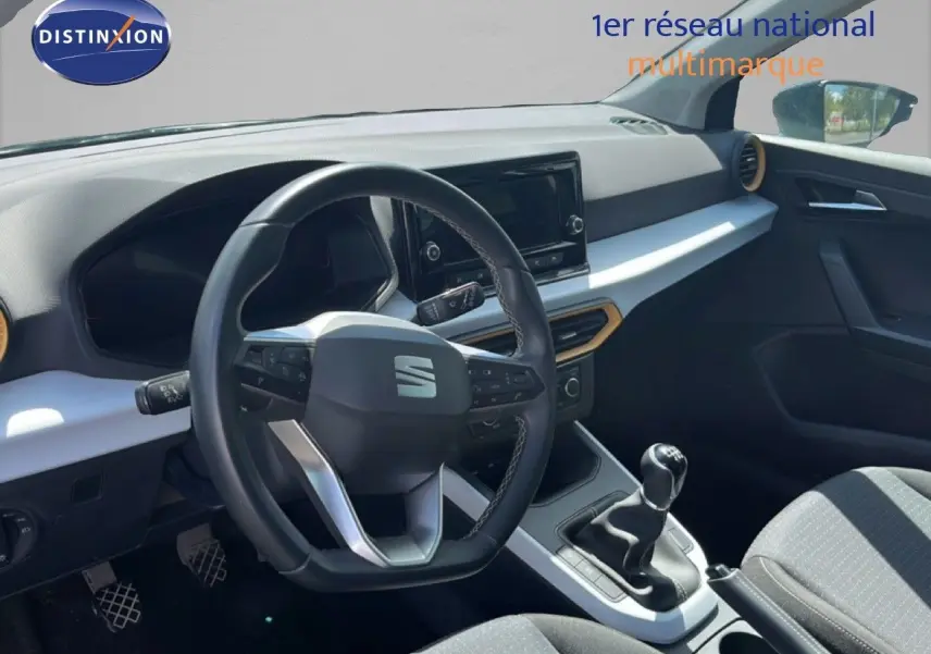 Vue intérieure du poste de conduite de la SEAT Arona bleu Fjord, volant multifonction et levier de vitesse manuel visibles.