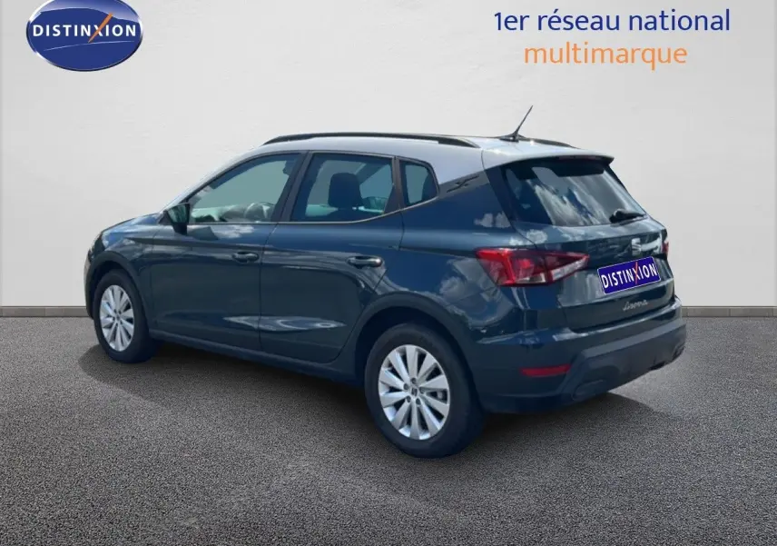 Vue 3/4 arrière droite d'une SEAT Arona bleu Fjord avec toit blanc, stationnée sur sol gris devant un mur clair.