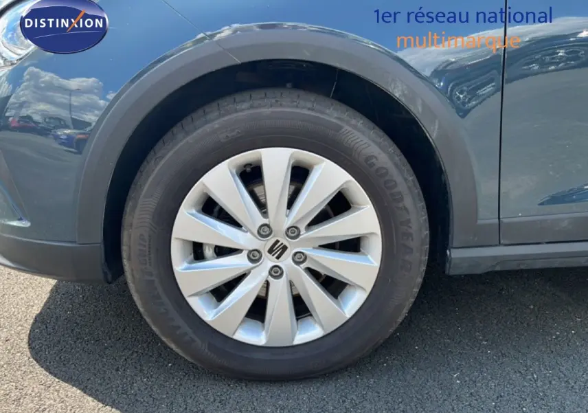 Gros plan sur la roue avant gauche d'un SEAT Arona bleu Fjord avec jante alliage et logo central SEAT.