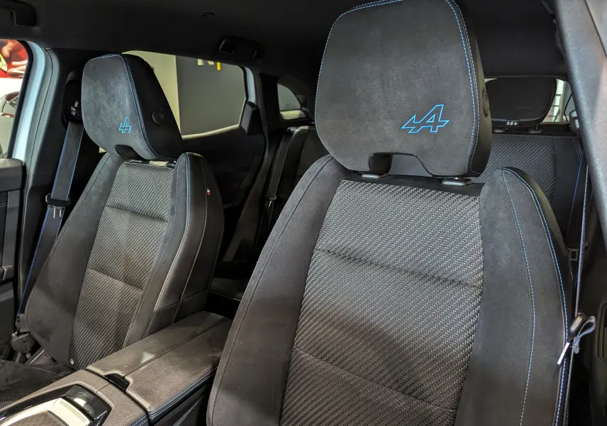 Vue rapprochée des sièges avant noirs avec surpiqûres bleues et logo Alpine brodé dans l'habitacle du Renault Austral 2023.