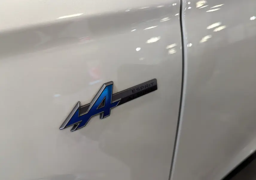 Gros plan sur l'écusson bleu "Esprit Alpine" sur la porte blanche nacrée du Renault Austral 2023.